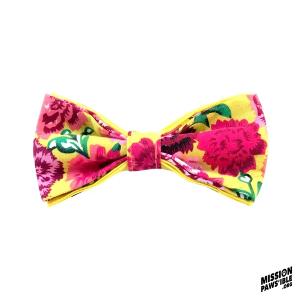 Presenting the Flower Power Yellow Bow Tie: a vibrant accessory showcasing pink and red flowers set against a bright yellow base, all on a simple white backdrop. The distinctive "Mission Pawsible" logo graces the bottom right corner.