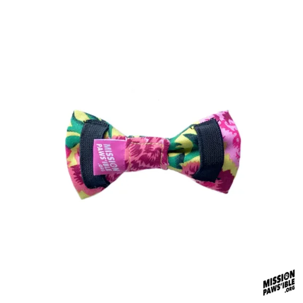 A vibrant bowtie adorned with floral patterns in pink, green, and yellow, labeled "Mission Pawsible," named the Flower Power Yellow Mini Bow Tie.