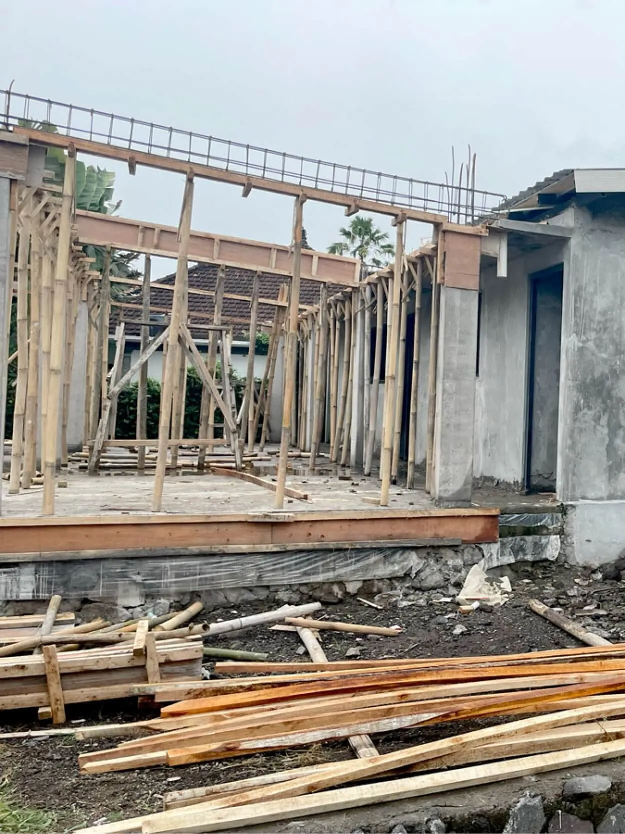 Partially constructed building with wooden scaffolding and piles of lumber on the ground.