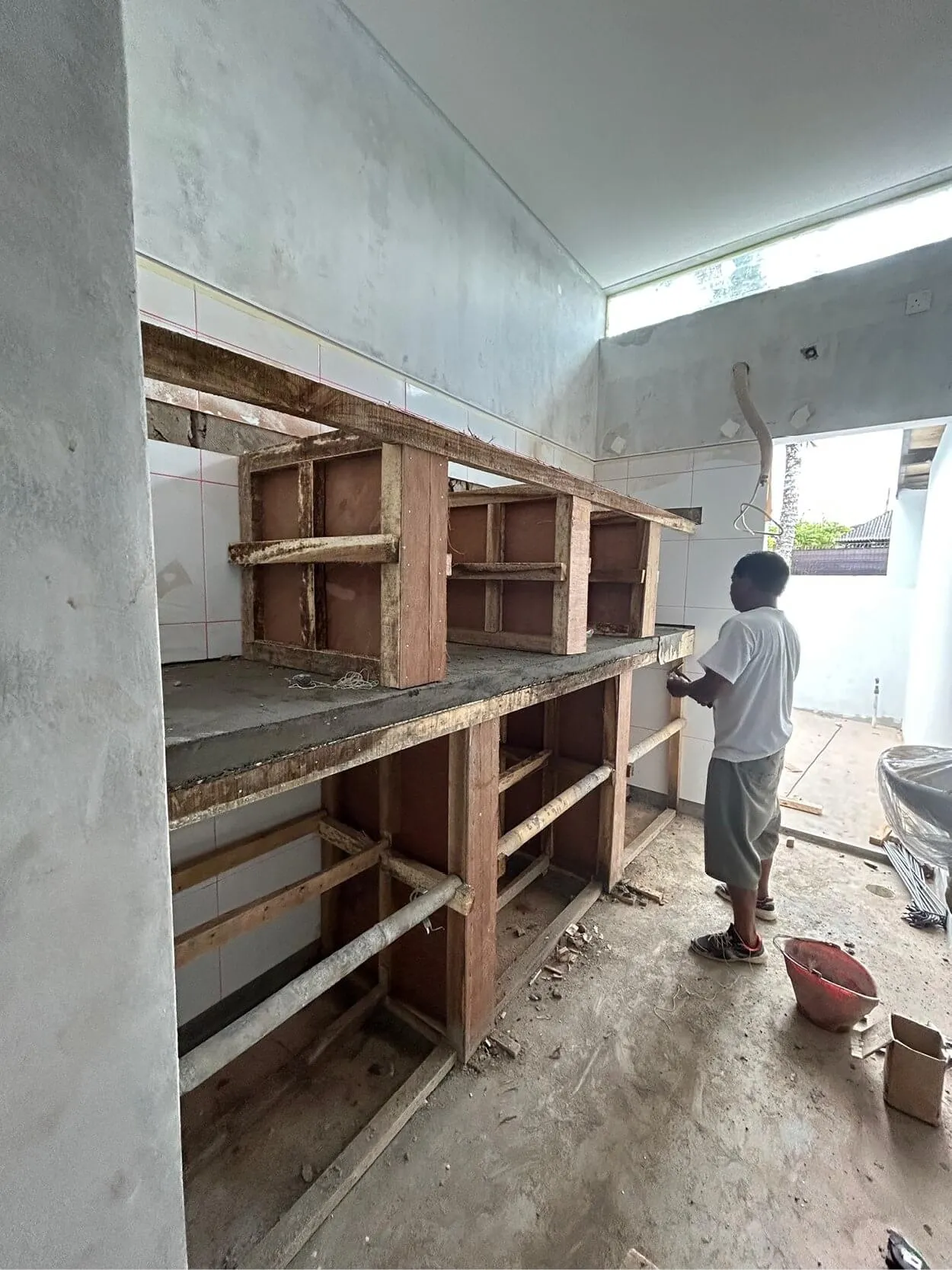 A person is working on constructing wooden shelves in a partially built room. There are tools and construction materials scattered on the floor.