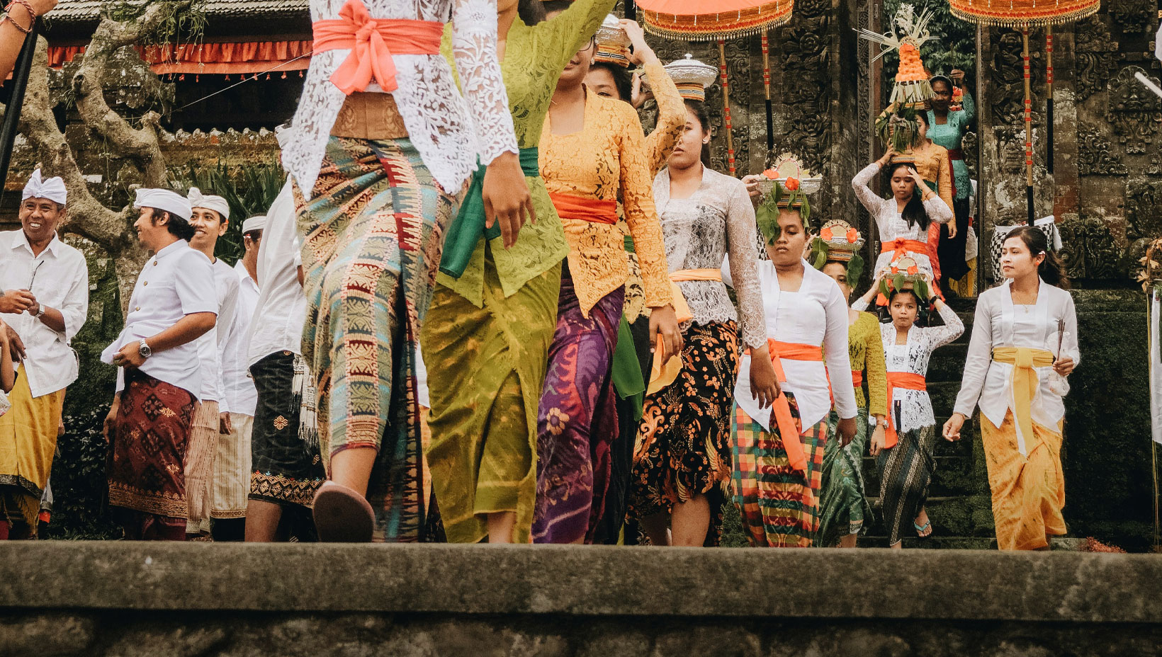 A group of people in traditional attire participates in a cultural procession outside a temple.